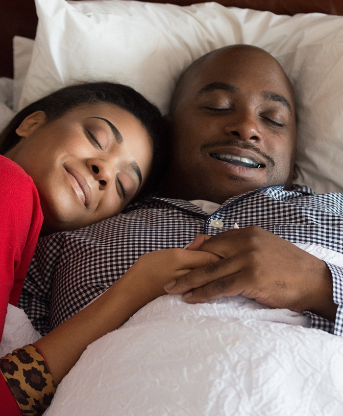 Man with sleep apnea oral appliance and his wife sleeping soundly