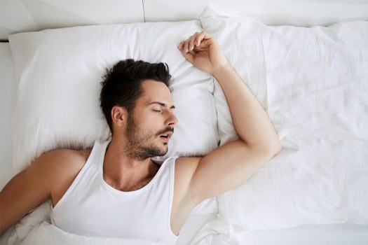 : Man in white tank top asleep in white bedding